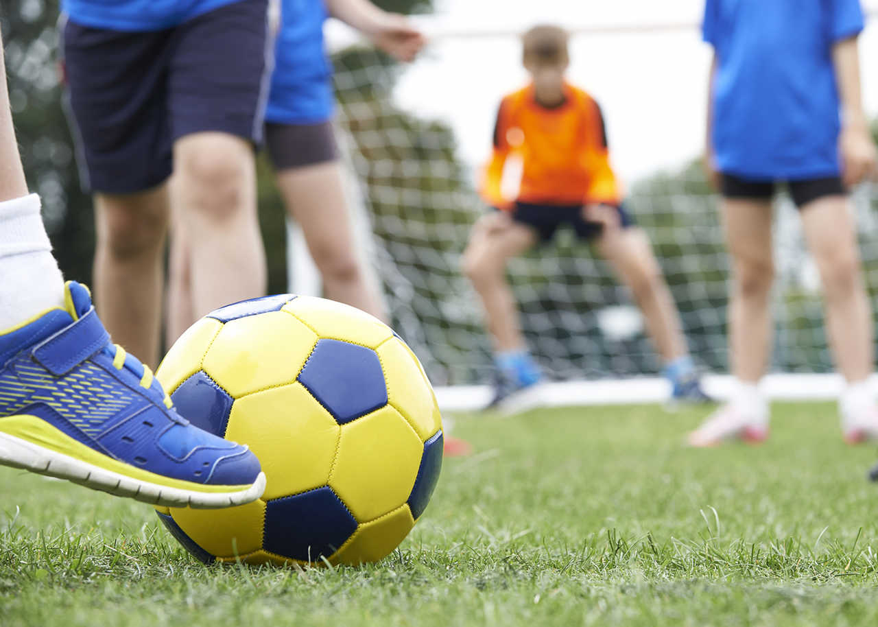 profissional-de-educacao-fisica-salario - pé na bola de futebol em maio a campo com crianças